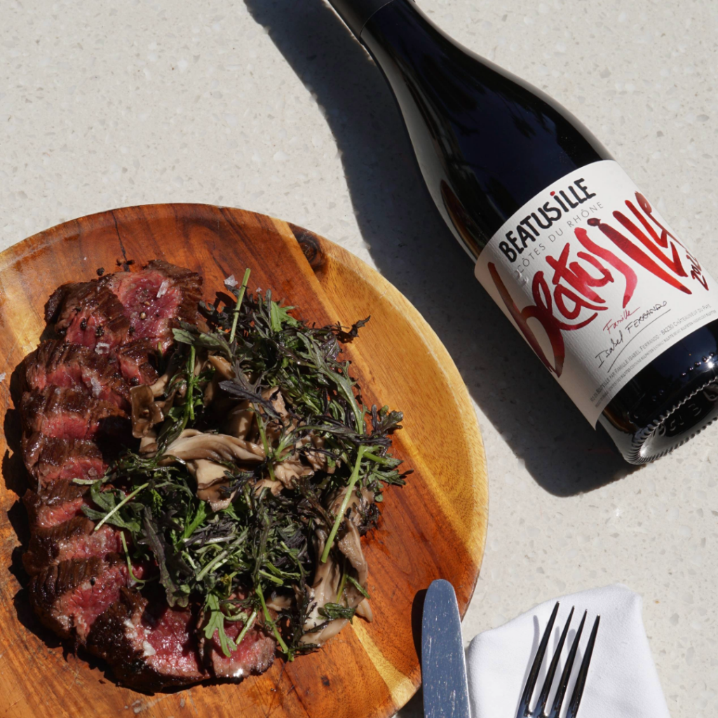 a plate of grilled steak served medium rare with a bottle of red wine